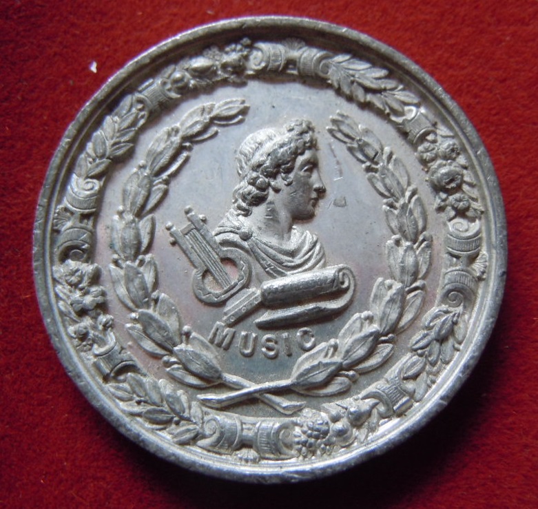 A Polished Aluminium Medallion - Obverse: A bust and lyre within two wreaths.  Reverse: The