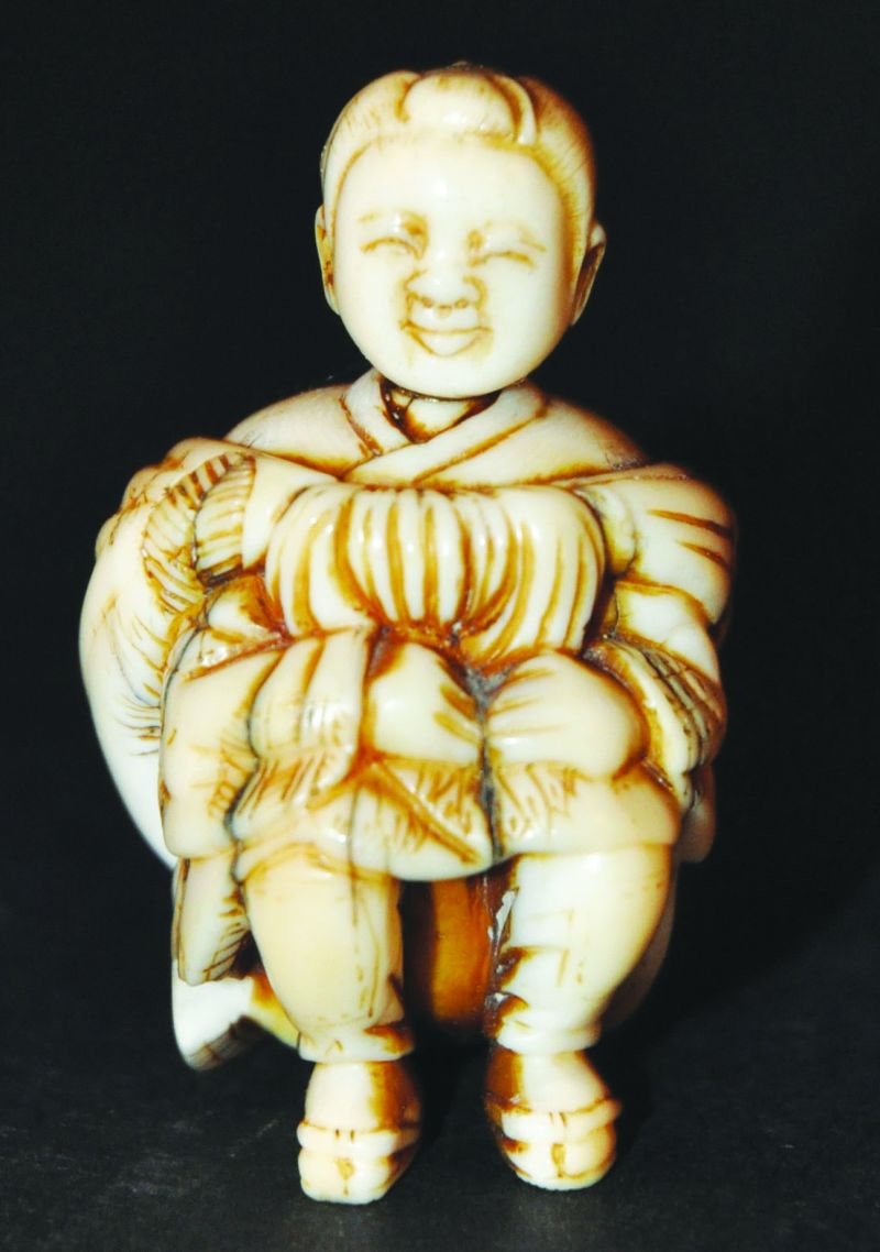 A SIGNED 19TH/20TH CENTURY JAPANESE NETSUKE, of a squatting boy draped in a bulbous cloak, 2in