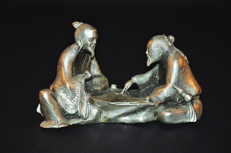 A CHINESE SILVERED-METAL MODEL OF TWO SAGES, seated and playing a board game, 7in wide.