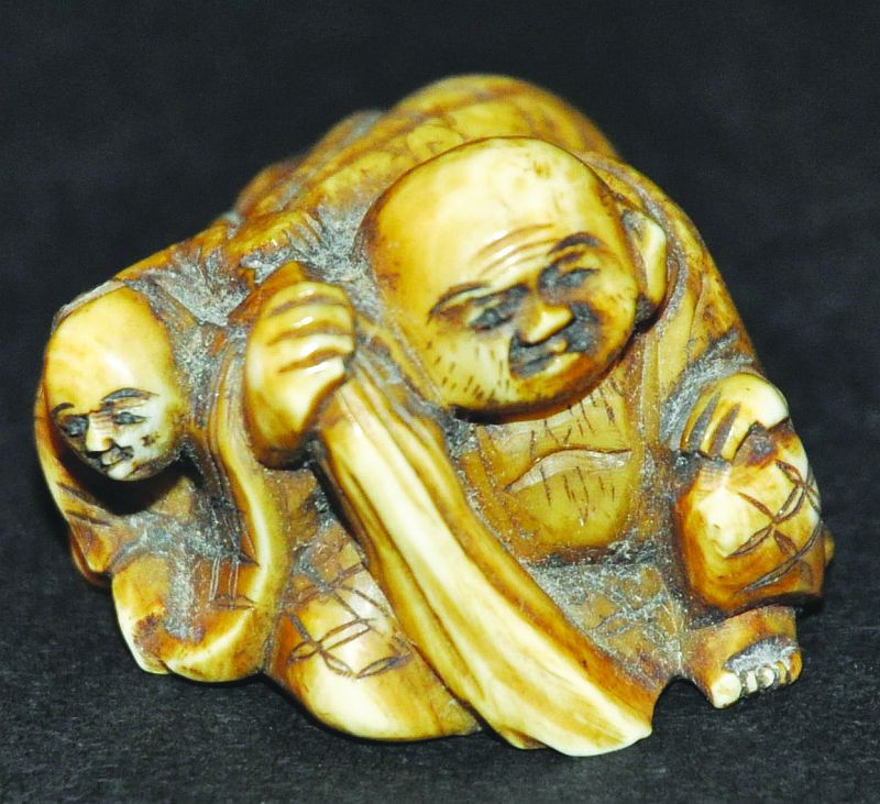 A SIGNED JAPANESE BONE IVORY NETSUKE OF HOTEI, circa 1900, holding his bag and in the company of a