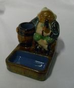 Royal Doulton Lambeth match stand/ashtray, modelled as a man smoking a pipe, leaning on a barrel