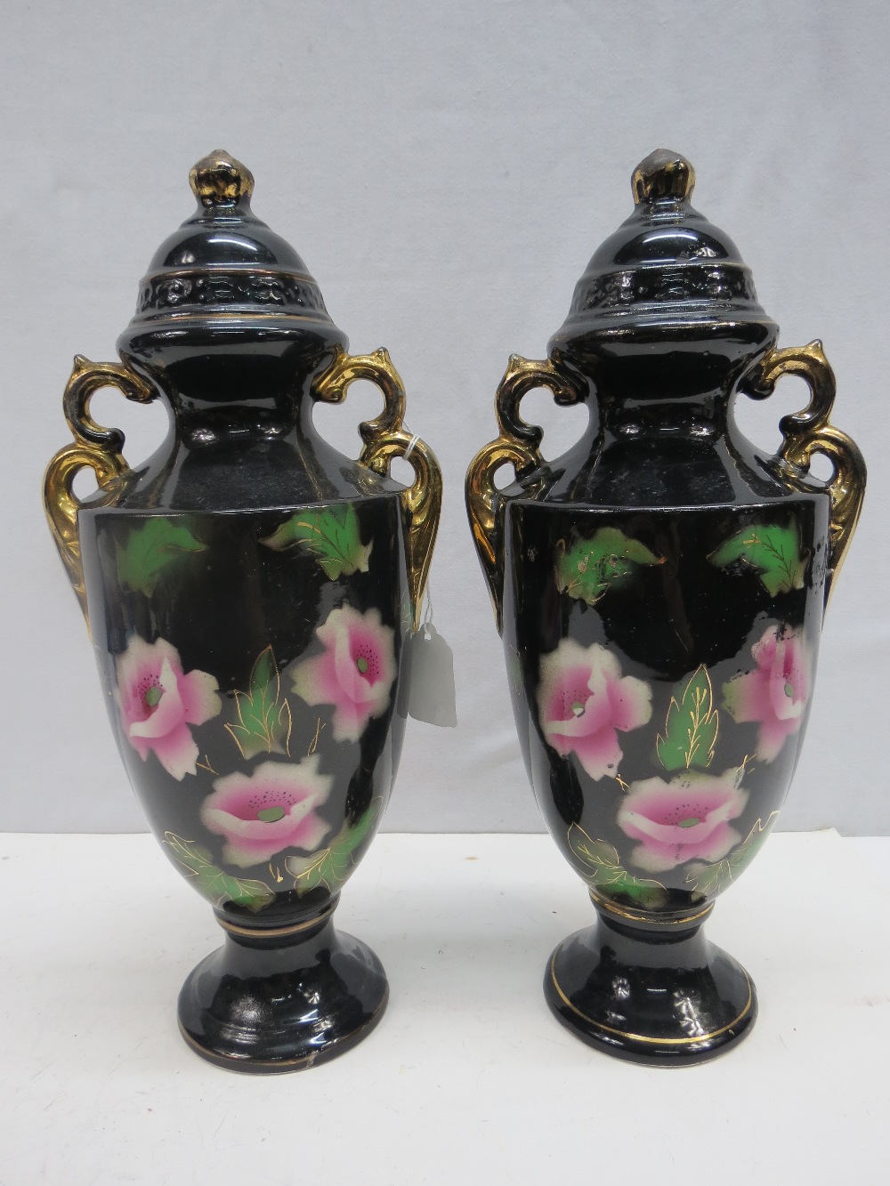 A pair of Edwardian style black glazed twin gilt handled urns, decorated with roses, each 36cm