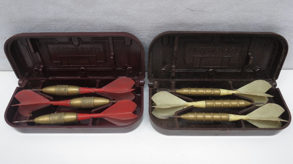 Two sets of vintage Unicorn darts with their bakelite boxes, one with white the other with red