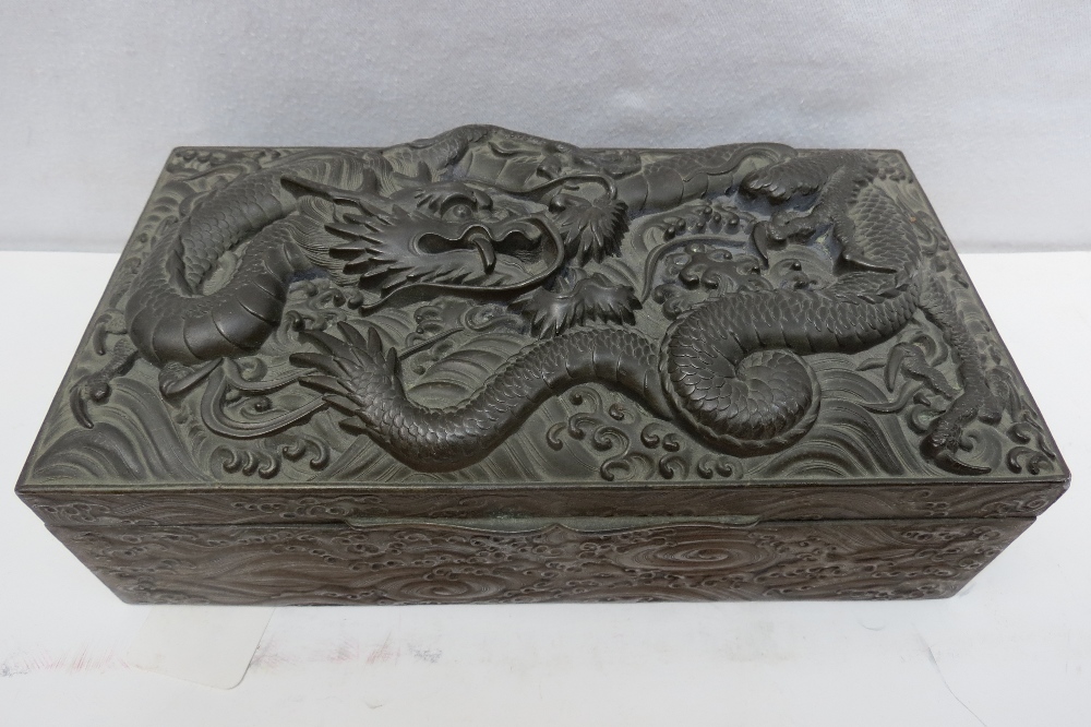 A Japanese bronze cigar box, the lid depicting a dragon on high relief, the sides ornamented with