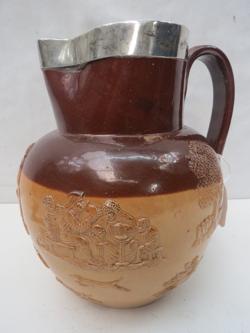 A large Doulton Lambeth Stoneware harvest jug with a hallmarked silver rim, dated 1892-3, 20cm.