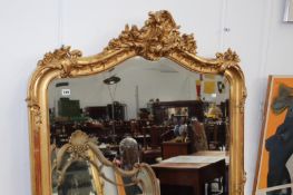 A LARGE ANTIQUE GILT FRAMED OVERMANTLE MIRROR WITH SHAPED BEVELLED PLATE