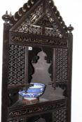 AN EASTERN CARVED AND EBONISED FLOOR STANDING CORNER CABINET WITH INCISED SCRIPT