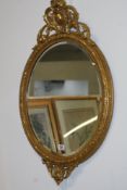 AN OVAL GILT WALL MIRROR WITH CARVED CREST AND A PAIR OF GILDED WALL SCONCE