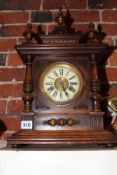 A GERMAN FOURTEEN DAY STRIKE MANTEL CLOCK IN CARVED WALNUT CASE WITH TURNED FINIALS.