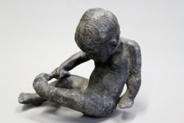 A lead figure of a young child removing their sock.