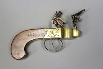 A brass flintlock tinder lighter, the frame decorated with a basic stand of arms to either side,