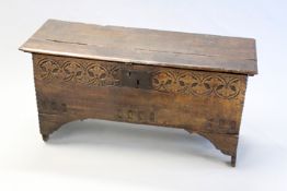 An early 18th Century oak plank coffer with plain top above carved decoration to the front panel,