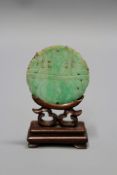 A 10k gold mounted Chinese jade medallion, 5.5cm diameter, on carved and pierced hardwood stand.