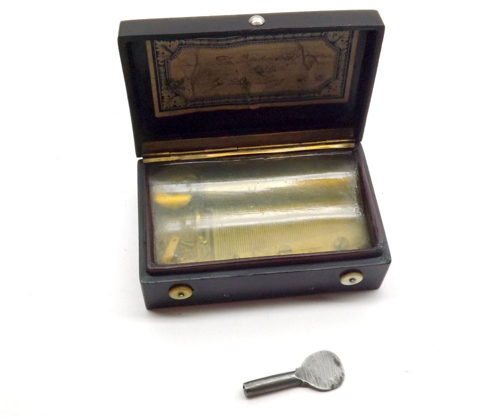 A small Pocket Musical Box in an embossed Bakelite Case, the lid decorated with a titled scene of ?