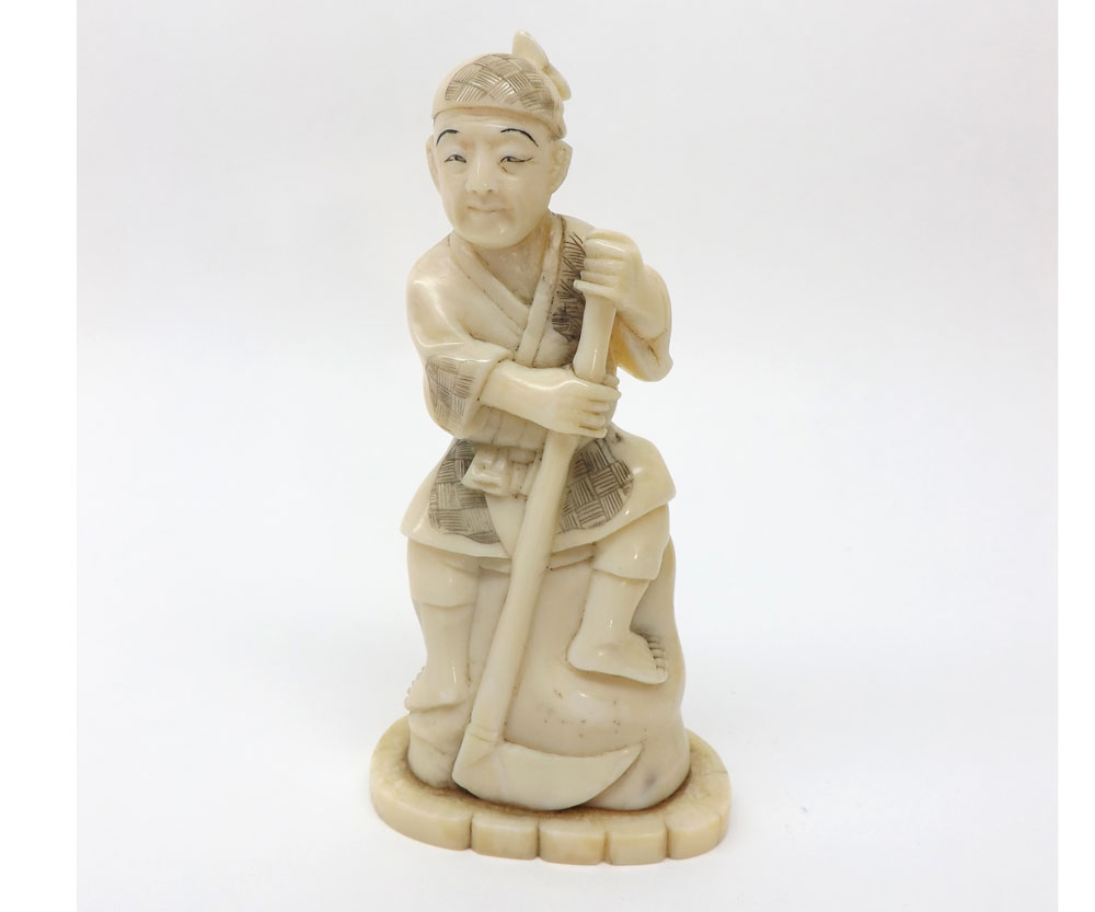 A small carved Ivory Okimono Figure depicting a seated worker with a scythe, 4 ½? high