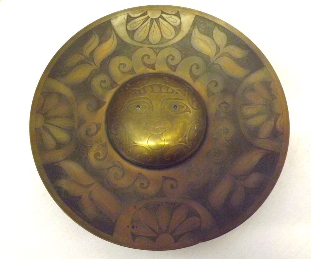 An unusual Circular Brass Plaque, the centre decorated with a roundel depicting a mask in the
