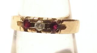 An unmarked yellow metal Ring set with small central Diamond and two red stones