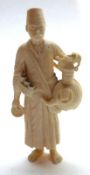 An Egyptian Ivory Figure, carved in the form of a liquor seller, wearing a turban and with jug and