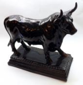 A large Dark Brown Glazed Pottery Model of a bull, raised on a rectangular plinth base, 15” long (