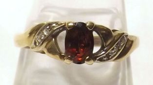A hallmarked 9ct Gold Red Stone Ring with Diamond chip shoulders, to a pierced setting