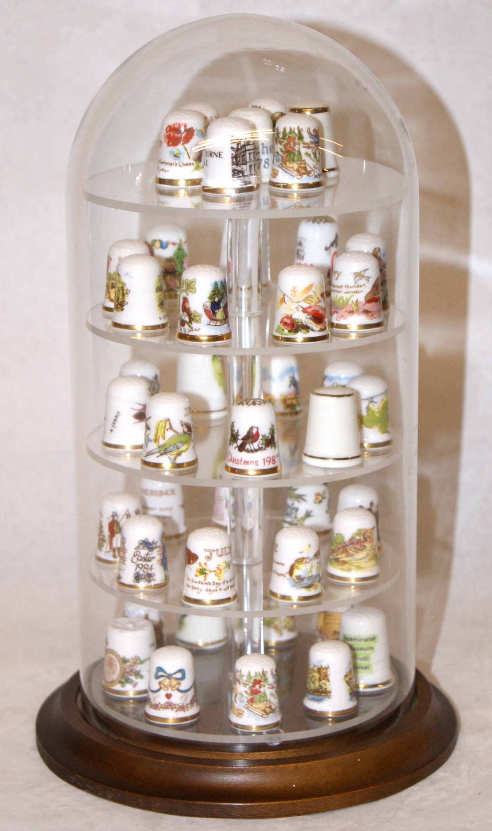 Collection of ceramic thimbles, together with display stand and glass dome.