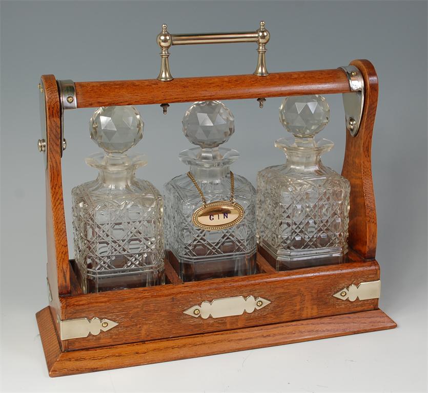 A circa 1900 oak and silver plated tantalus, having three square decanters and stoppers, w.37cm