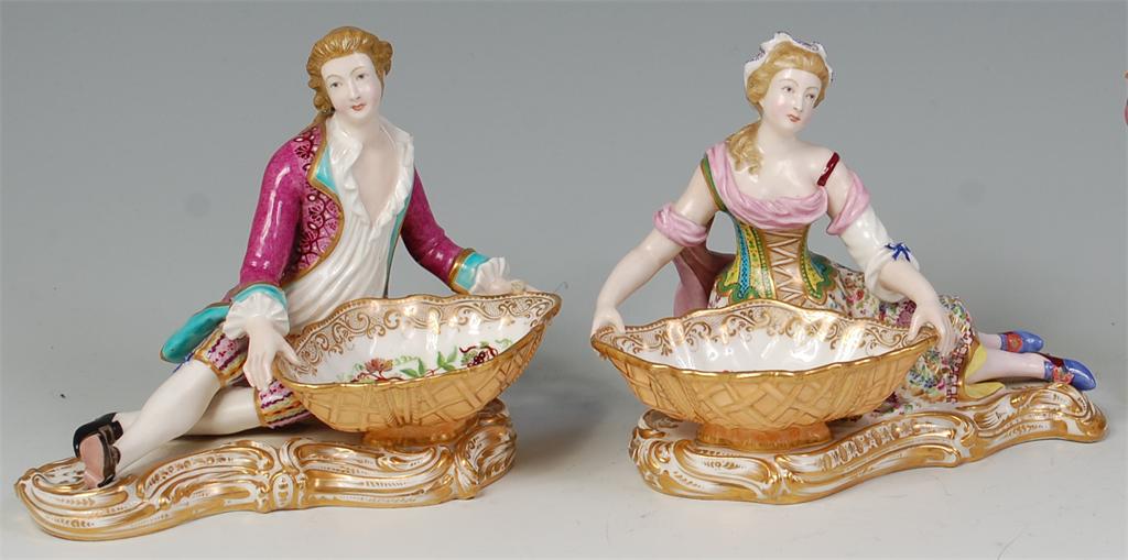 # A pair of 19th century porcelain figural table salts, modelled as a reclining couple in 18th