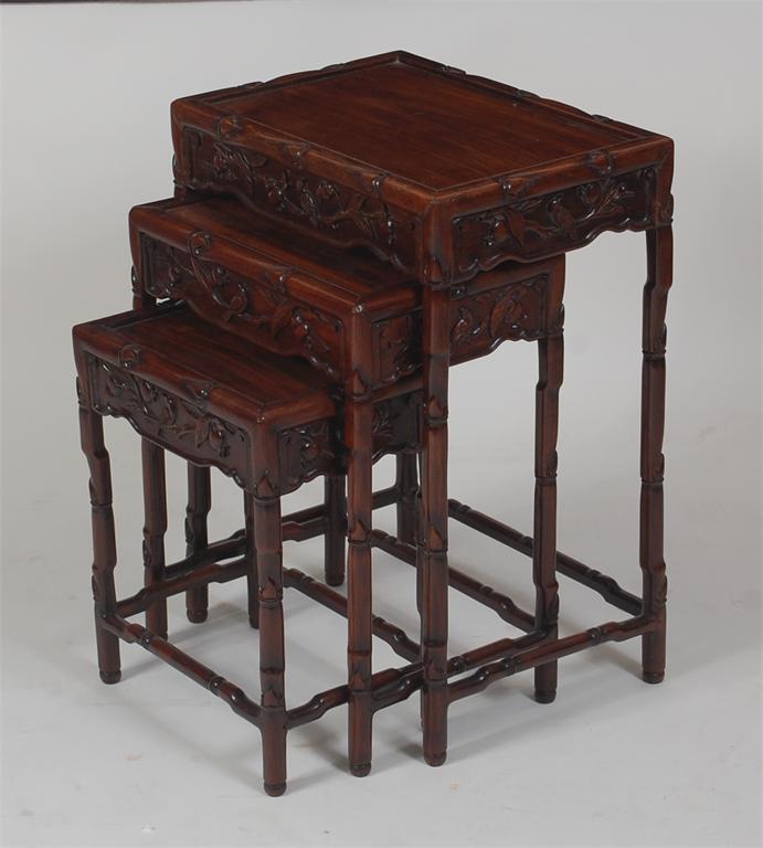A Chinese carved 'rosewood' nest of three occasional tables, each with dish tops and on faux