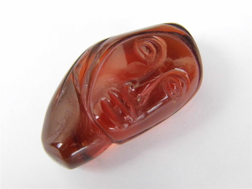 An amber nodule carved in depiction of a scarved female visage, 48 mm