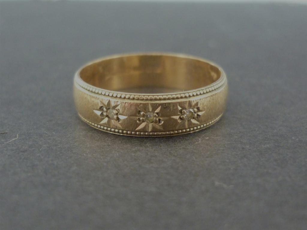 A 9ct gold and diamond band, having three gypsy set brilliants reserved within a millegrain border