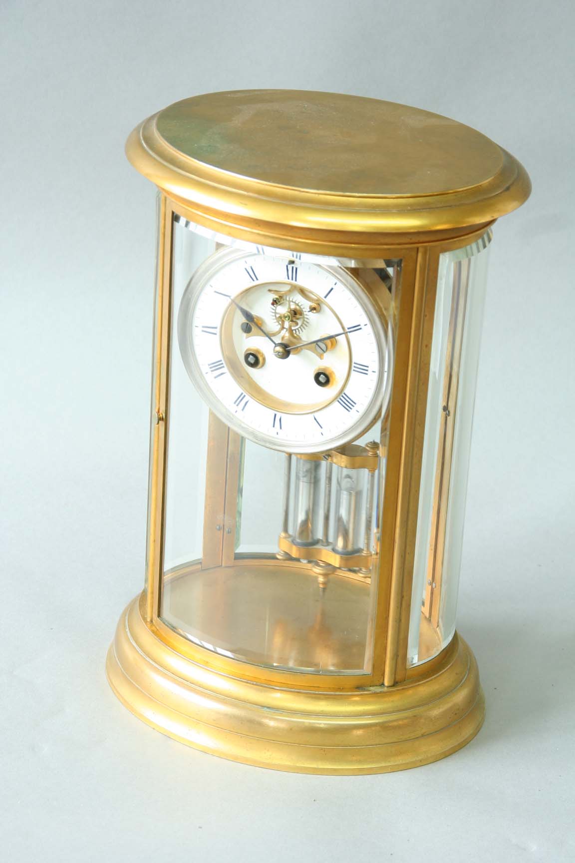 AN ORMOLU OVAL FOUR GLASS MANTEL CLOCK dial white enamel, movement drum, exposed escapement with