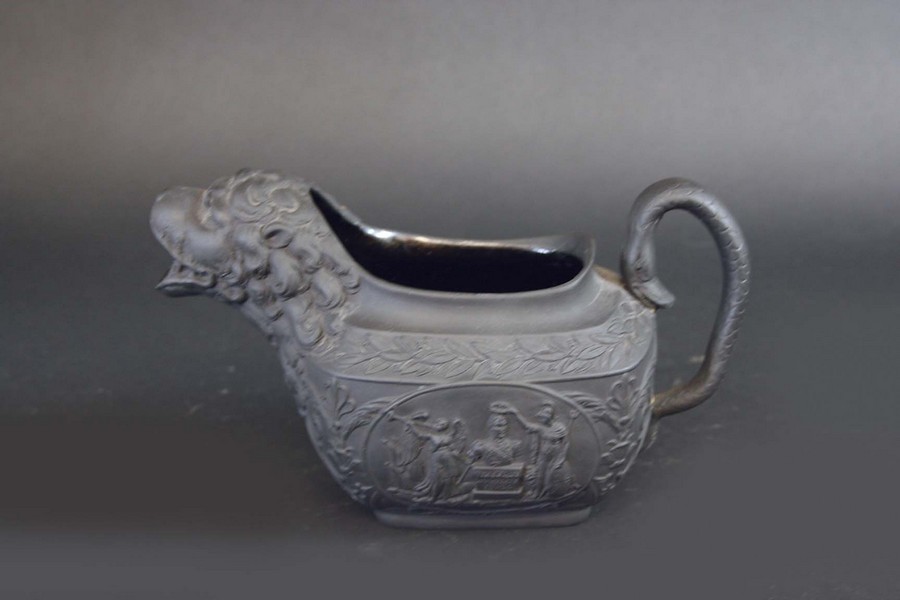 A BLACK BASALT WELLINGTON CREAM JUG one side moulded with a bust on a pedestal, the reverse