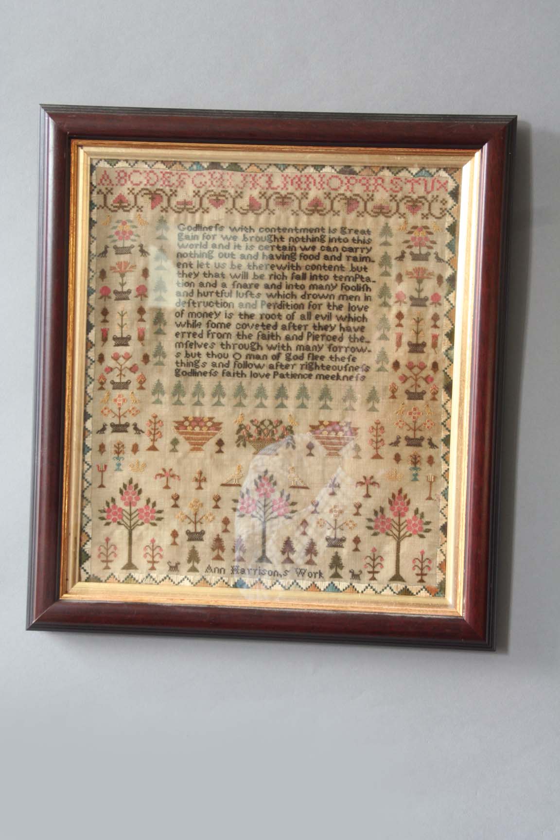 A NEEDLEWORK SAMPLER worked with a text and flowering plants by Ann Harrison, 13ins.(33cms.) x 11