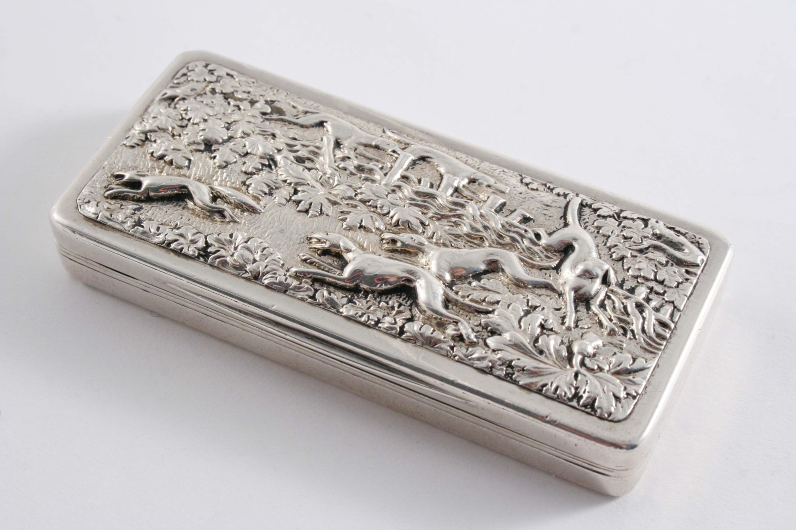 A GEORGE IV SHALLOW OBLONG SNUFF BOX decorated in relief on the cover with hounds chasing a fox over