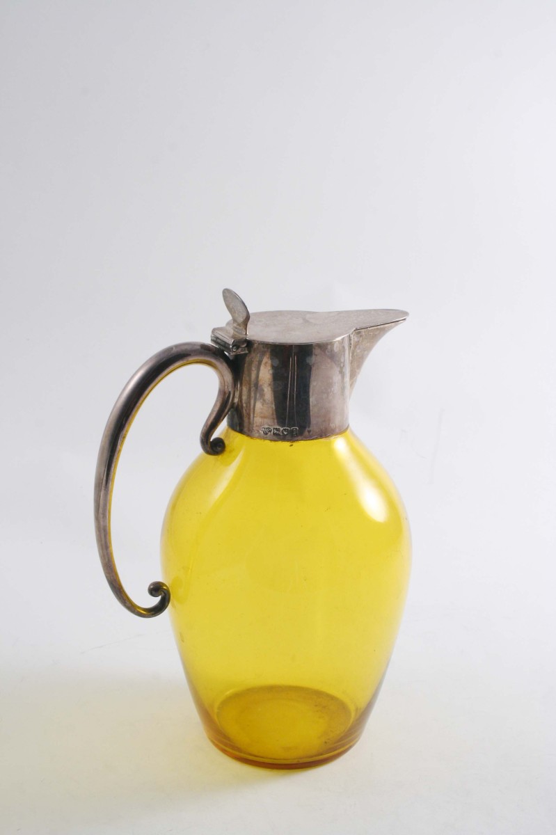 AN EDWARDIAN MOUNTED AMBER-COLOURED GLASS CLARET JUG with an oviform body & a c-scroll handle, by