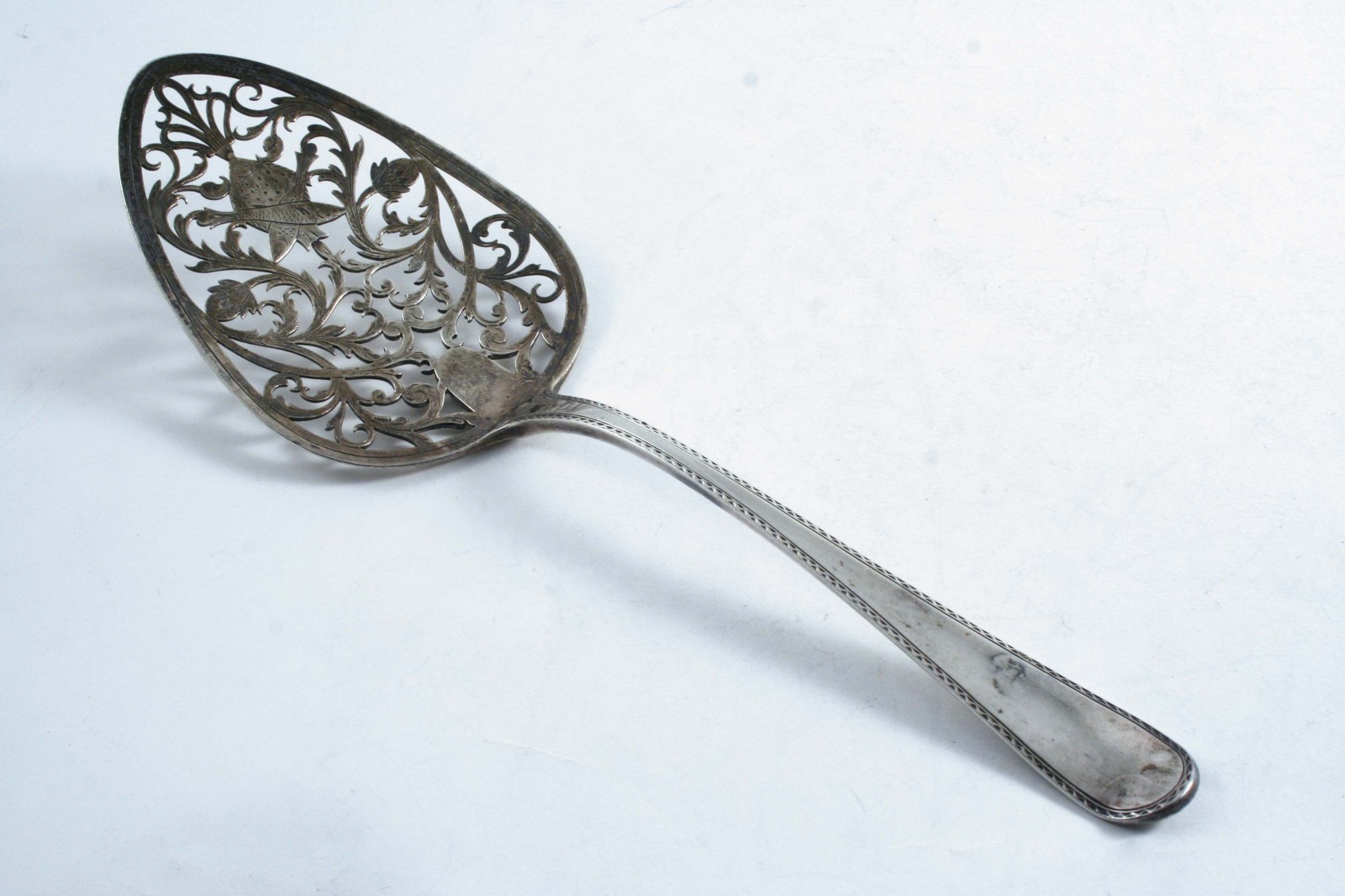 A GEORGE III FISH SLICE with a bright-cut bordered stem & a rounded, triform blade pierced &
