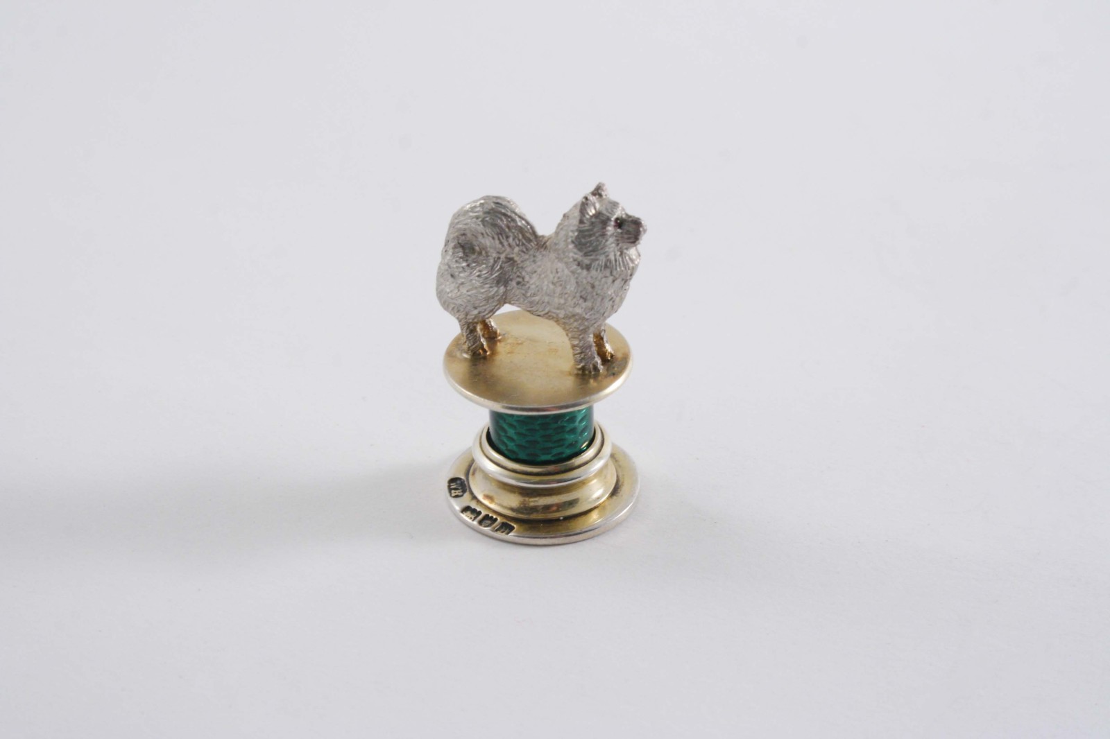 AN EDWARDIAN PARCELGILT & ENAMELLED SEAL in the form of a dog with gem-set eyes on a short green