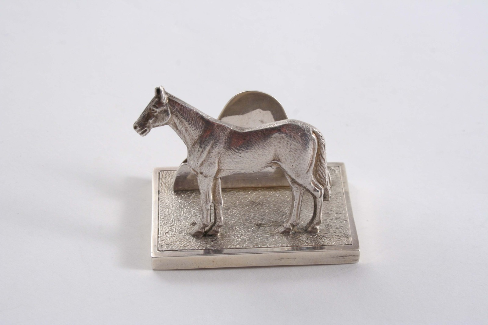 A MODERN CAST MENU HOLDER in the form of a horse standing on an oblong base, by the Goldsmiths &