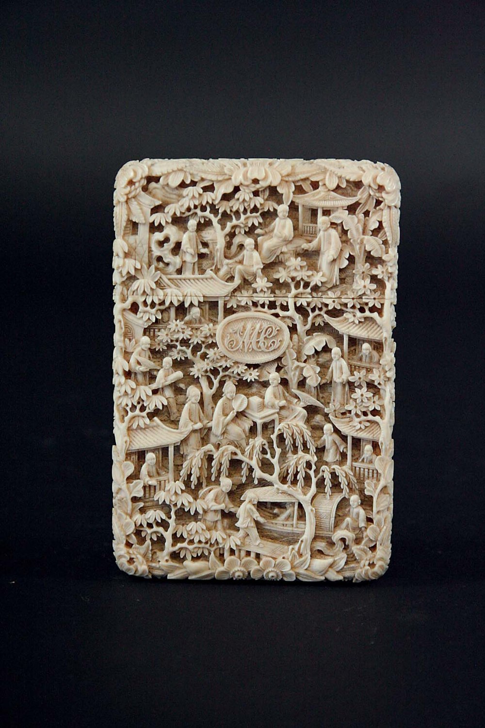 A CANTONESE IVORY CARD CASE deeply carved with a profusion of figures amongst trees and pavilions, M