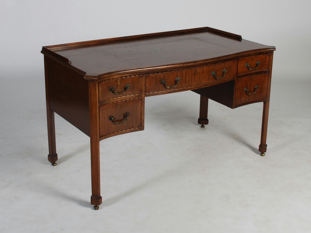 An early 20th century mahogany serpentine fronted desk, the shaped top with a slightly raised