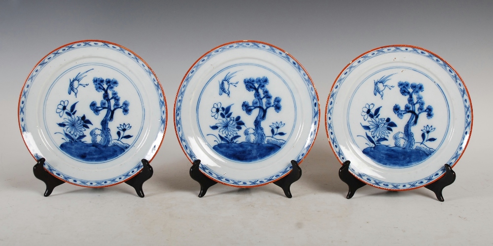 A set of three 19th century Delft plates, decorated with a garden of flowers, pine tree and bird,
