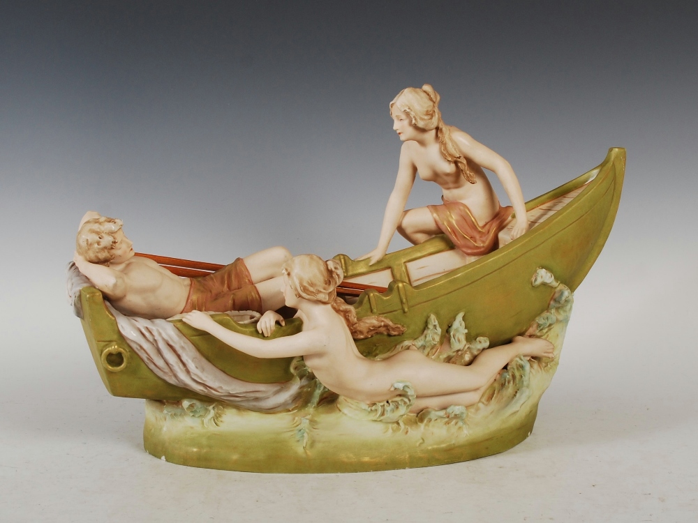 A Royal Dux porcelain figure group of a boy reclining in a fishing boat with two maidens, applied