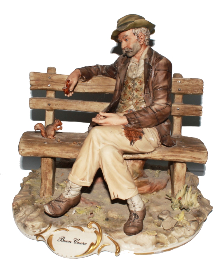 A Capodimonte figurine of a gentleman on a bench with squirrel, entitled `Buon Cuore` on a shaped