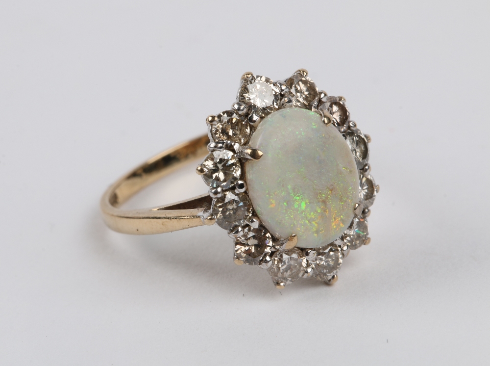 A 9CT GOLD RING with central oval opal flanked by a border of twelve diamonds