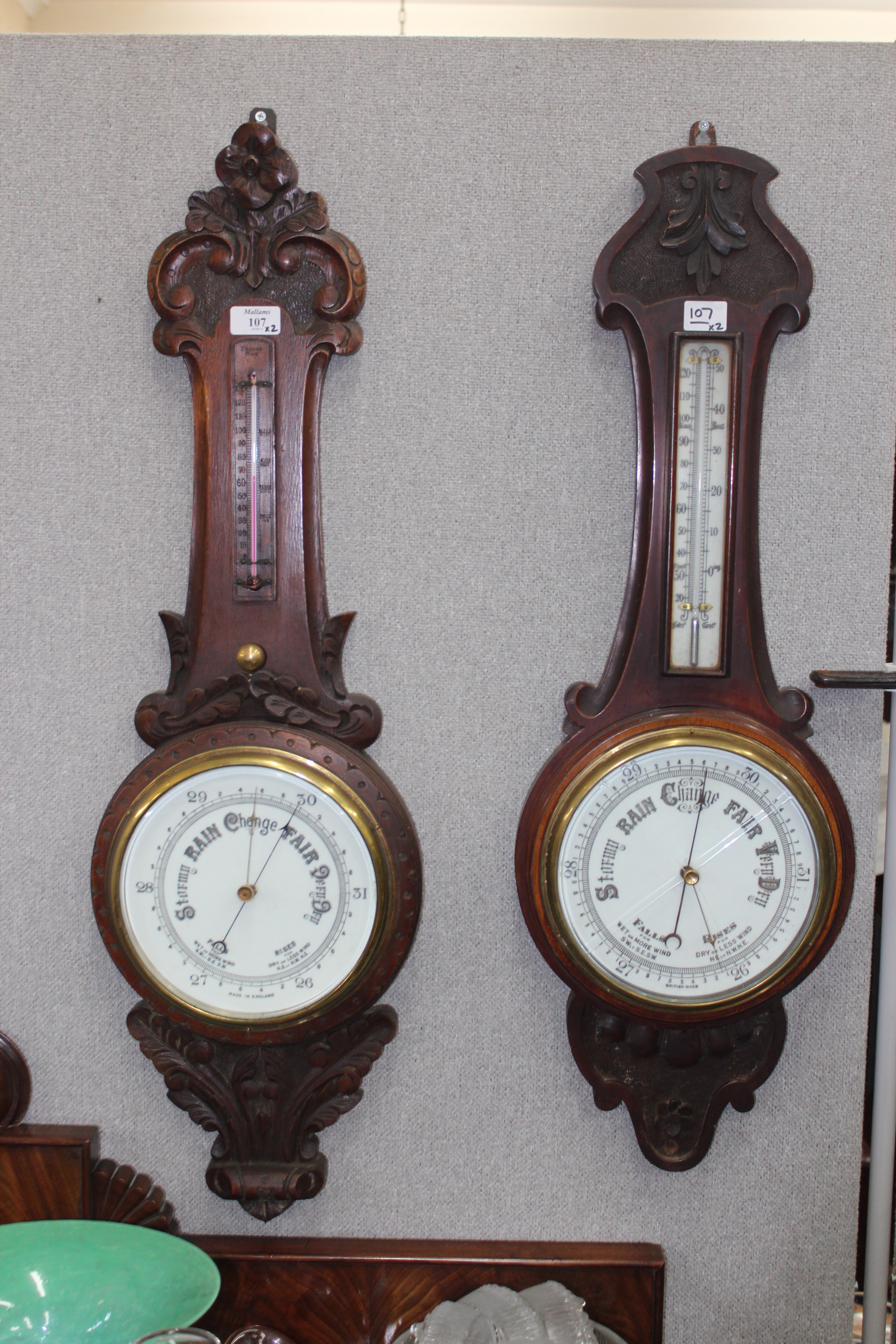 A CARVED MAHOGANY ANEROID WHEEL BAROMETER WITH A THERMOMETER  OVER, and a similar oak example (2)
