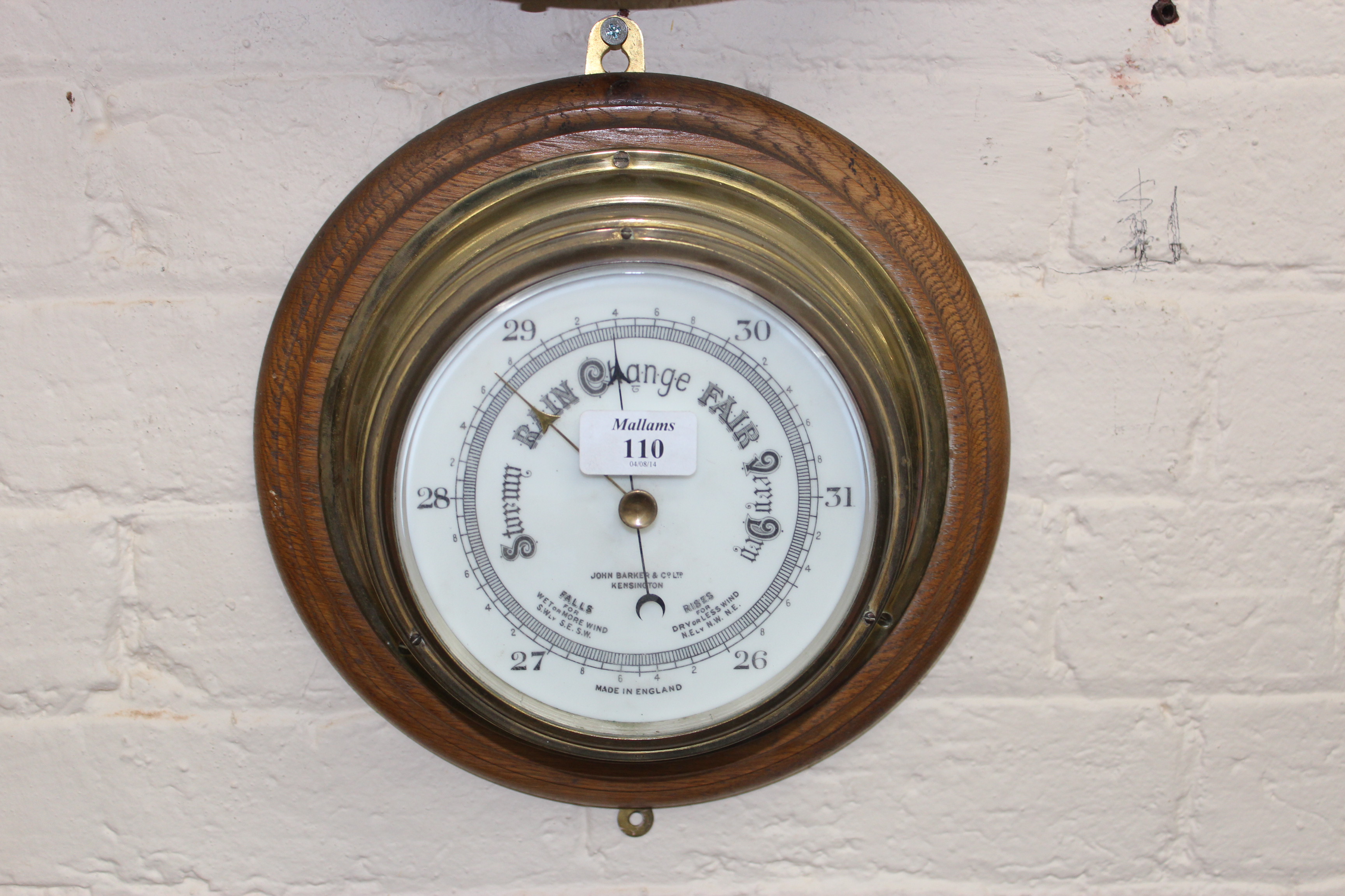 A BRASS SHIPS BULKHEAD ANEROID BAROMETER, the six inch ceramic dial, signed John Barker and Co.