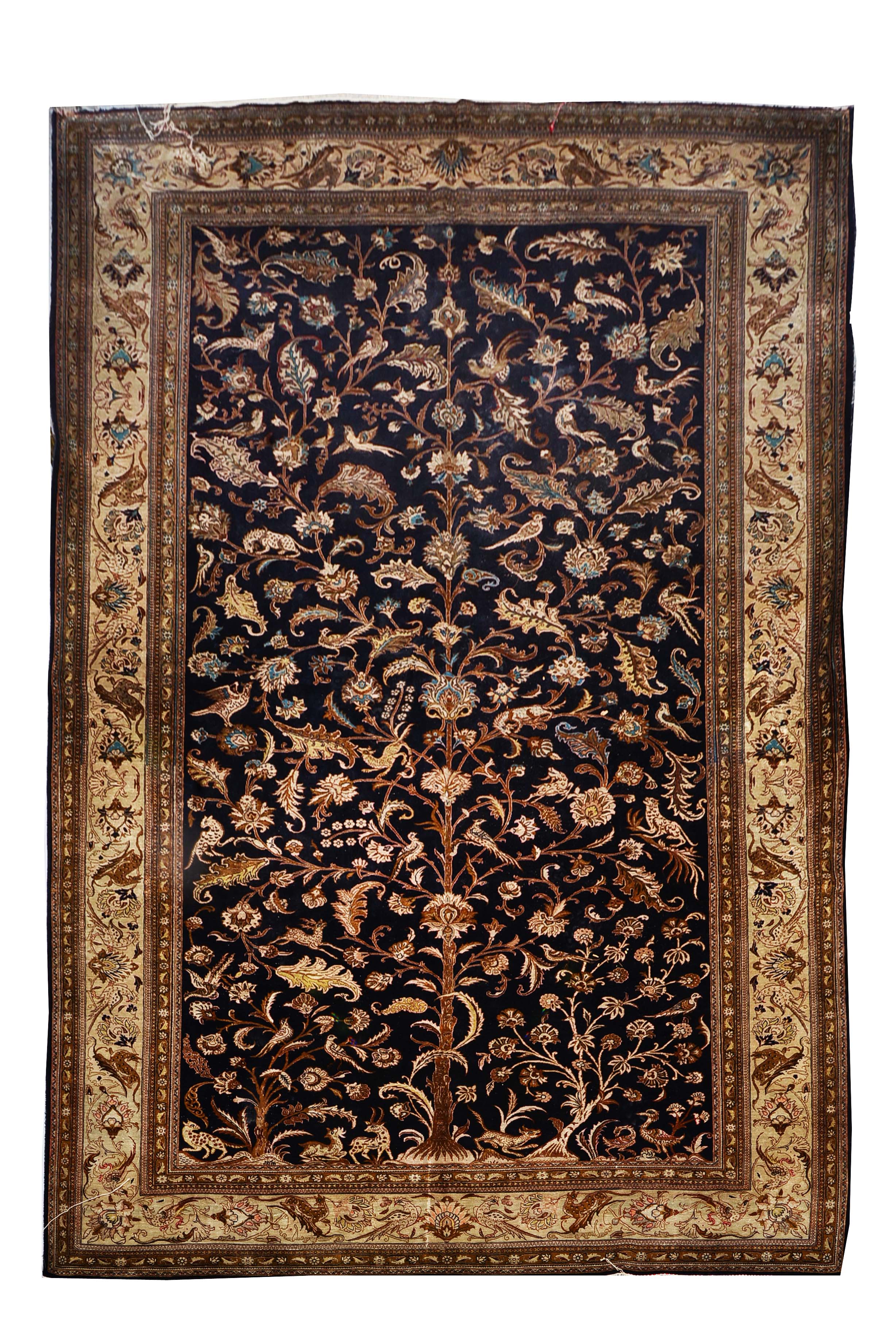 A PERSIAN QUM SILK RUG decorated with a central tree motif with birds, leopards and deer on a dark