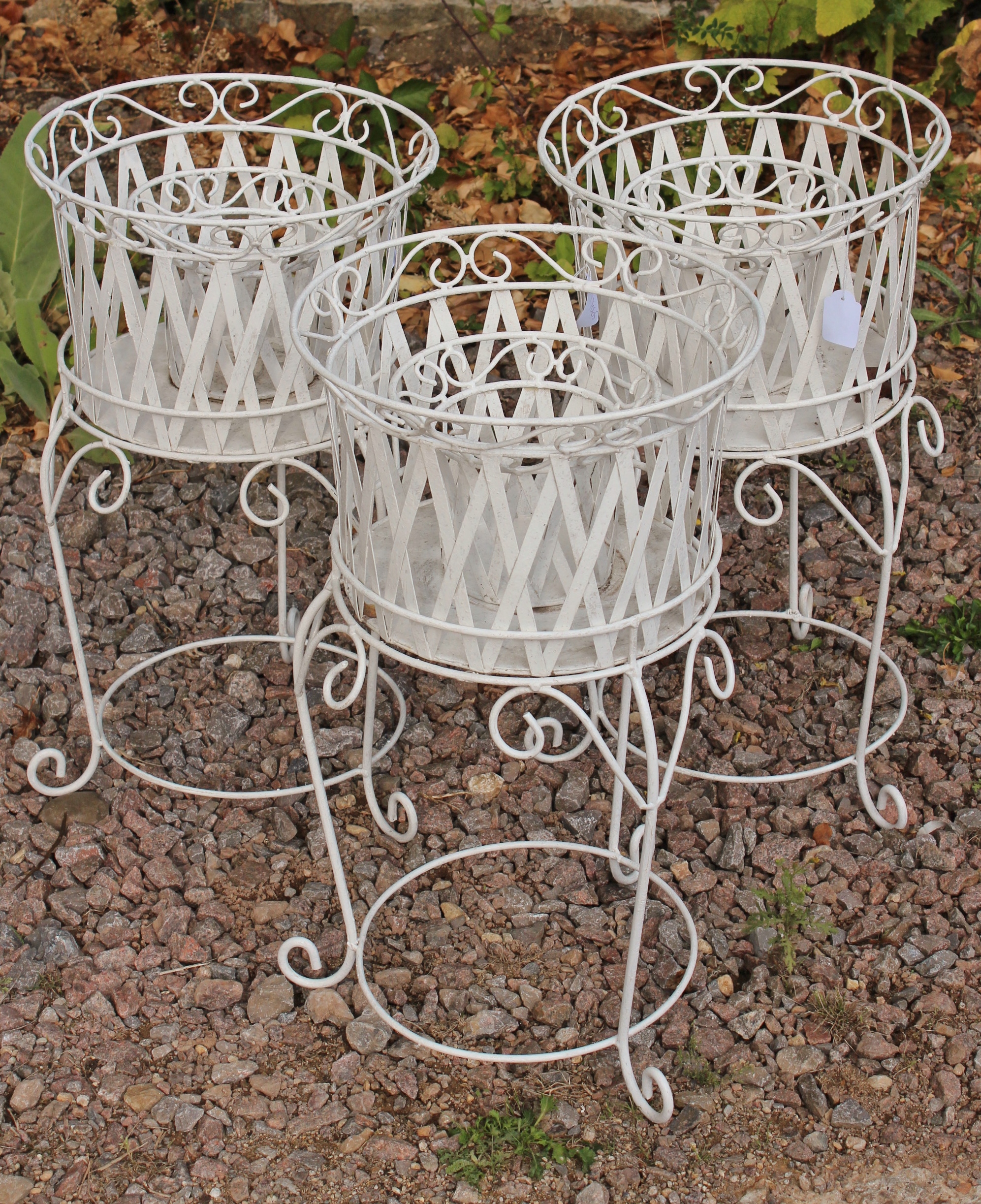 A SET OF THREE WHITE PAINTED WROUGHT IRON PLANTERS on stands with scroll and strap work decoration