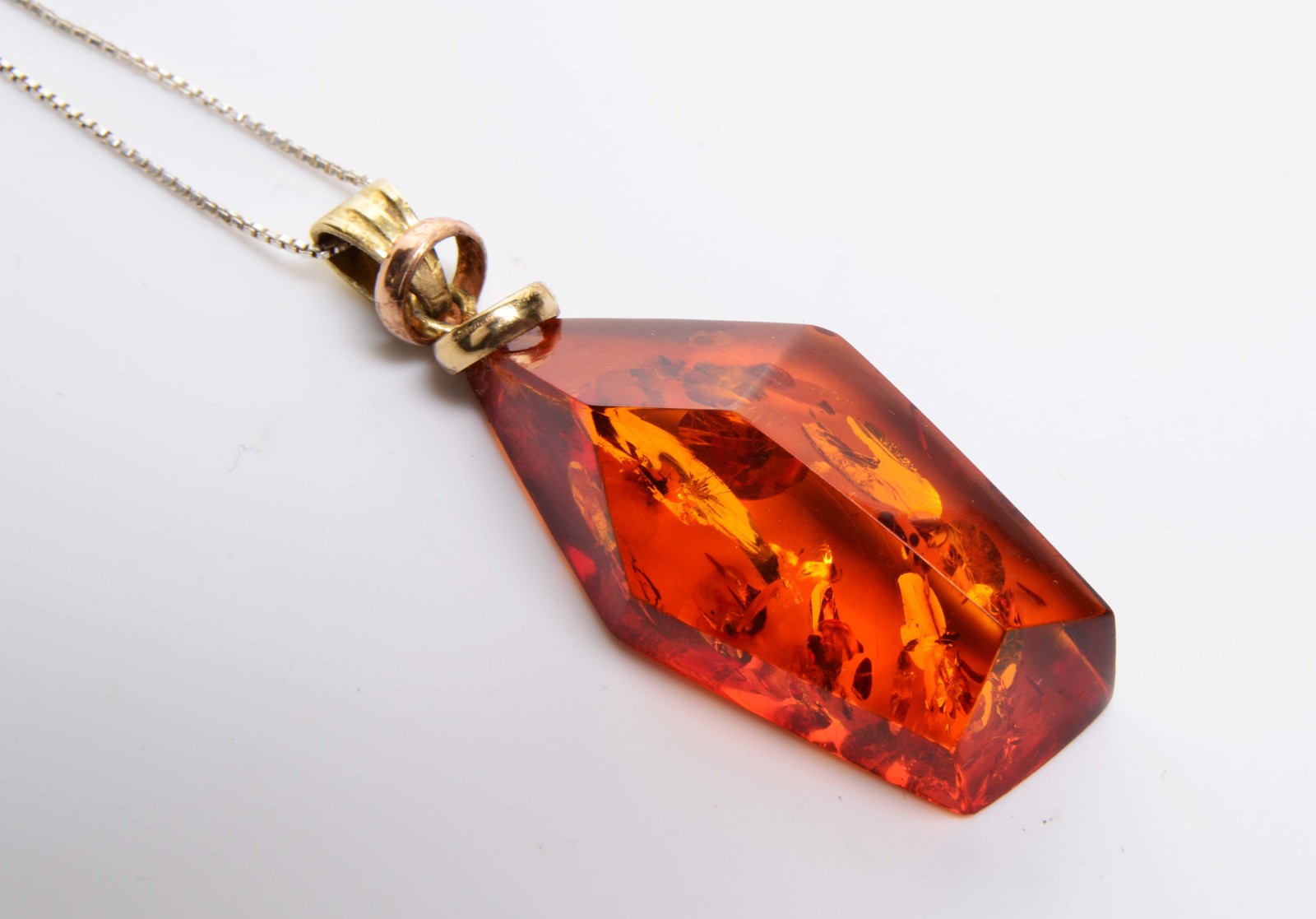 A FACET CUT AMBER PENDANT with an inset inclusion, 4cm in length, mounted on a silver chain