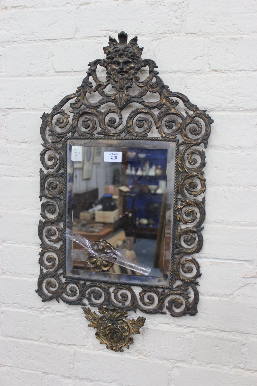 A 19TH CENTURY BRASS HANGING WALL MIRROR with bevelled glass, mask and scroll surround, 26" x 15"